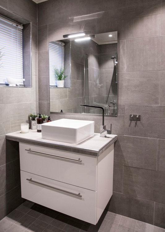 A bathroom with grey tiles floor to ceiling and a white vanity unit with a basin on top