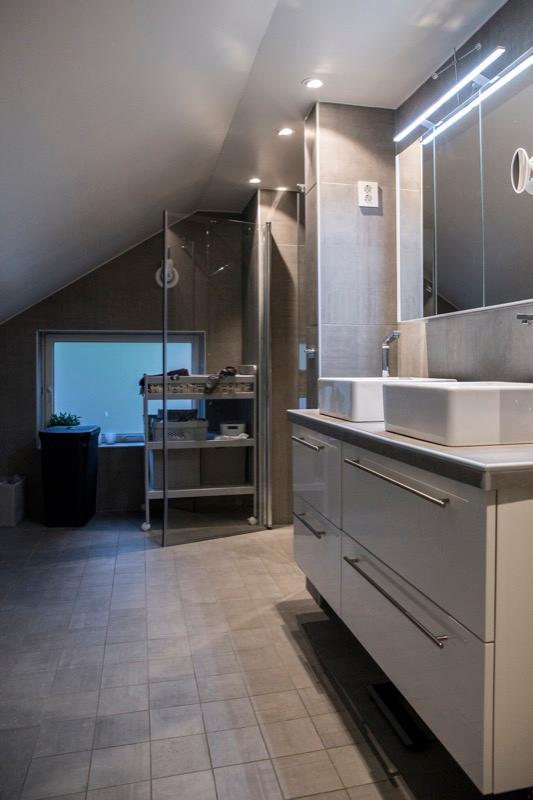 A bathroom under a sloping ceiling, grey tiles and a white vanity